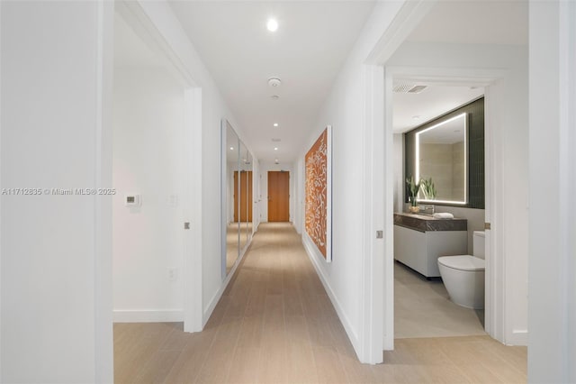 hall featuring baseboards, visible vents, light wood-style flooring, and recessed lighting