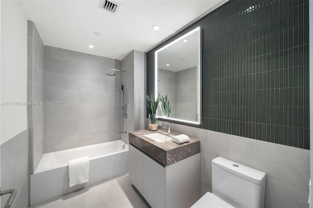 full bath featuring tile walls, visible vents, shower / bathing tub combination, toilet, and vanity