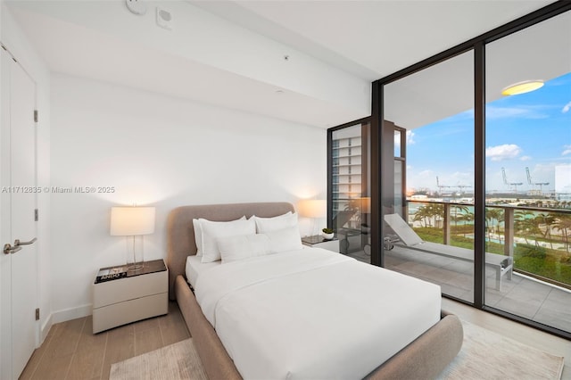 bedroom featuring access to exterior, floor to ceiling windows, baseboards, and wood finished floors