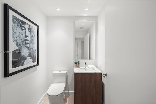 half bath with toilet, recessed lighting, baseboards, and vanity