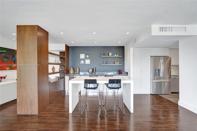 kitchen with appliances with stainless steel finishes, a kitchen breakfast bar, dark wood-type flooring, white cabinets, and a center island