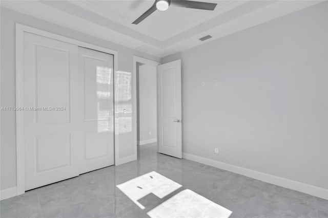 unfurnished bedroom featuring a tray ceiling, ceiling fan, a closet, and crown molding