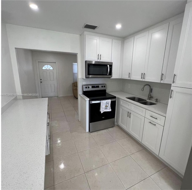 kitchen with white cabinets, sink, light stone countertops, light tile patterned floors, and stainless steel appliances