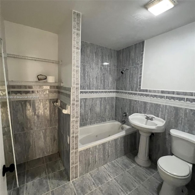 bathroom with tile patterned flooring, tiled shower / bath combo, toilet, and tile walls