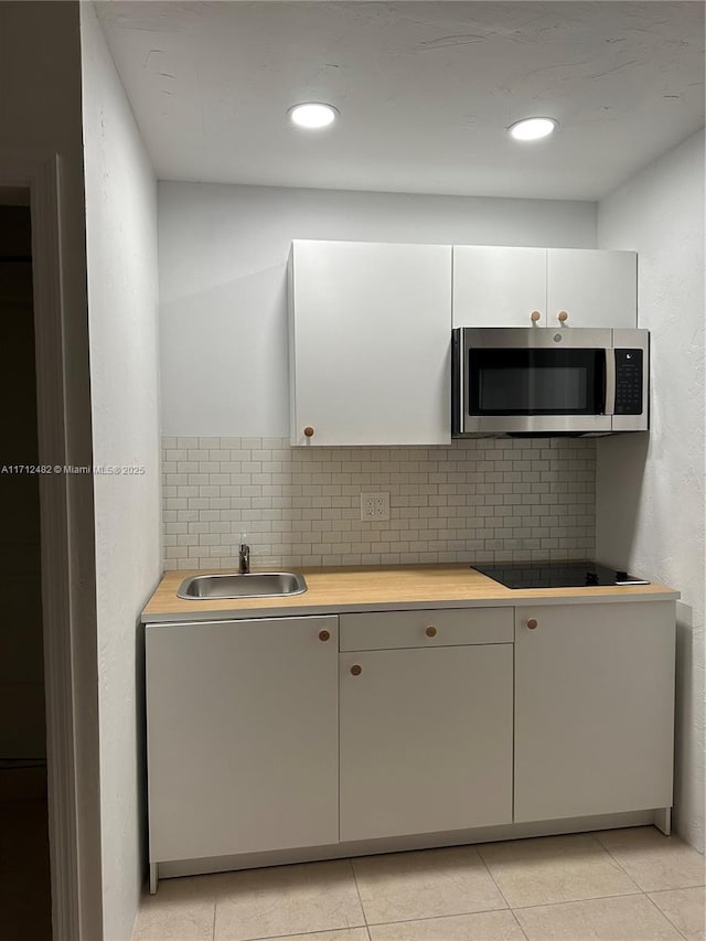 kitchen with light tile patterned flooring, sink, white cabinetry, black electric stovetop, and backsplash