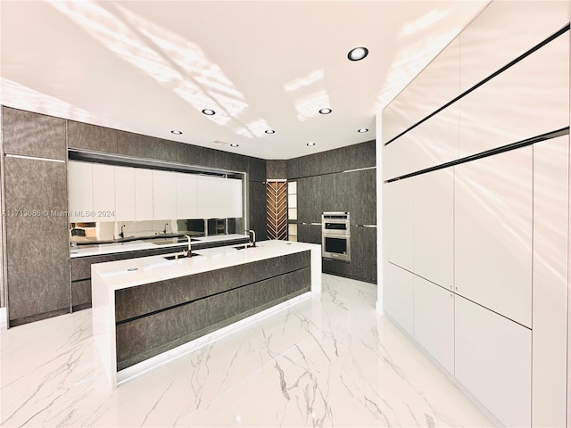 kitchen featuring white cabinetry, double oven, a kitchen island with sink, and sink