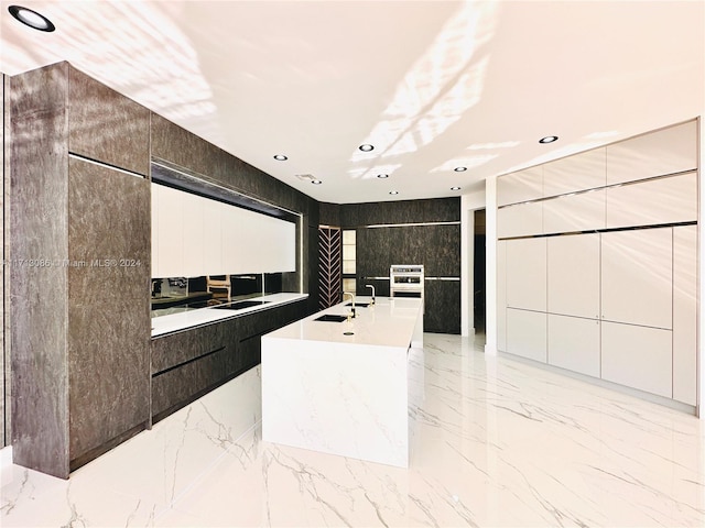 kitchen featuring light stone countertops, white cabinetry, tile walls, and an island with sink