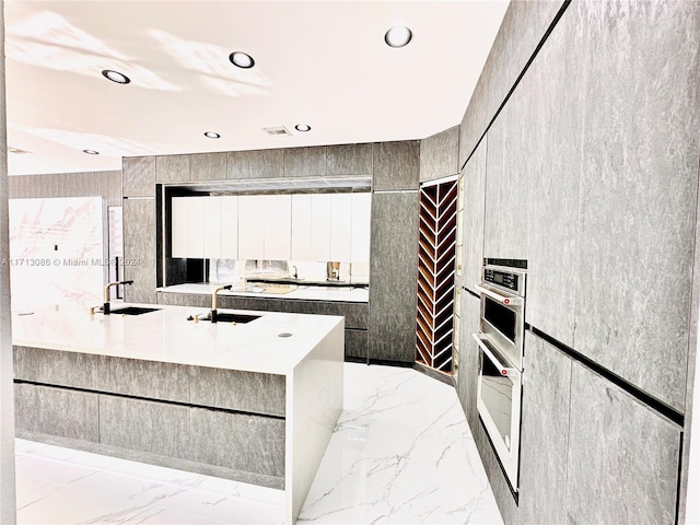 kitchen featuring a kitchen island with sink, double oven, and sink