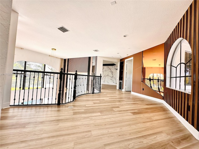 corridor with a textured ceiling and light hardwood / wood-style flooring