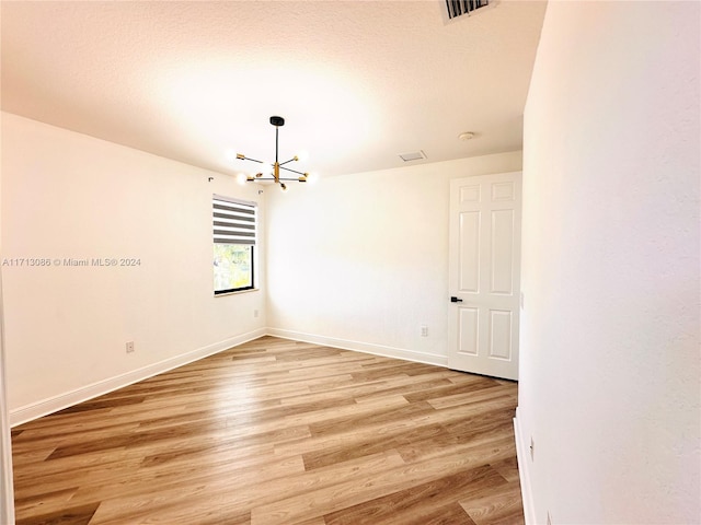 unfurnished room with a notable chandelier, light hardwood / wood-style floors, and a textured ceiling