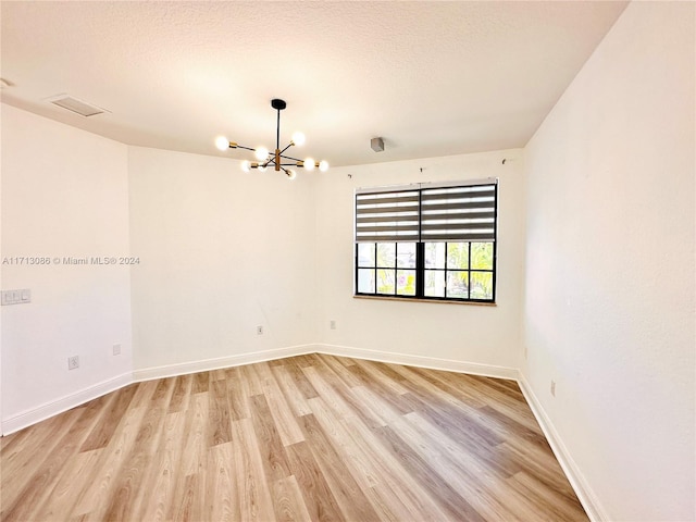 empty room featuring a textured ceiling, light hardwood / wood-style flooring, and a notable chandelier