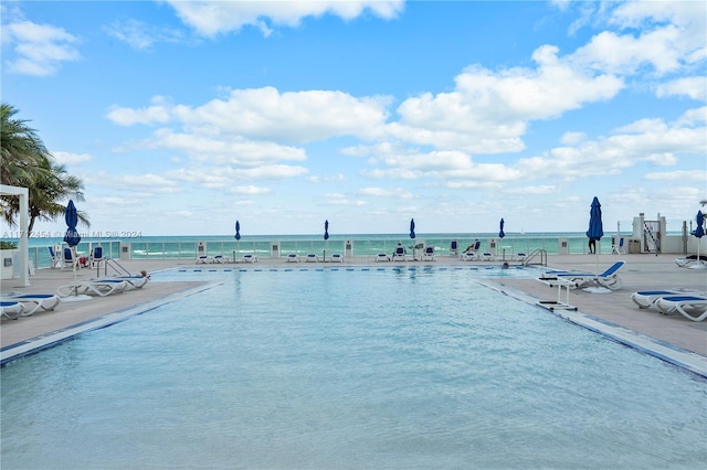 view of swimming pool featuring a water view, a patio, and a view of the beach