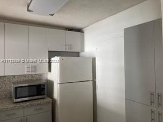 kitchen with white cabinets, light stone counters, and white fridge