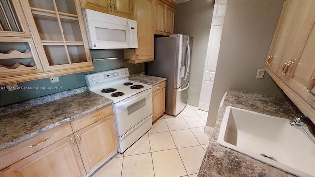 kitchen featuring dark stone counters, white appliances, sink, light tile patterned floors, and light brown cabinets