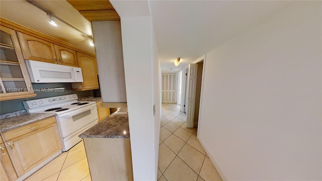 kitchen with light tile patterned floors, white appliances, baseboards, dark stone counters, and glass insert cabinets