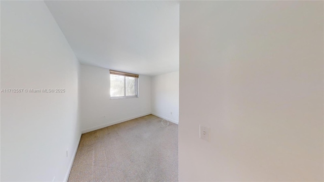 spare room featuring light carpet and baseboards