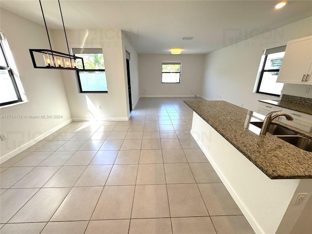 kitchen featuring sink, hanging light fixtures, light tile patterned floors, dark stone countertops, and white cabinets