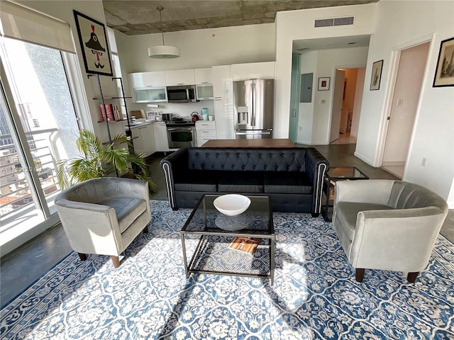 living area with a high ceiling, electric panel, visible vents, and finished concrete floors