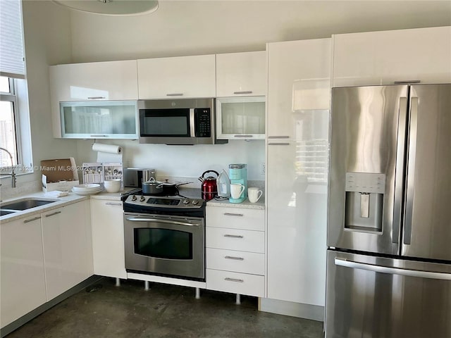 kitchen with light countertops, appliances with stainless steel finishes, white cabinets, a sink, and concrete floors