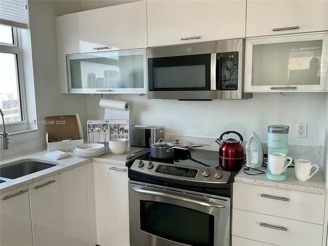 kitchen featuring appliances with stainless steel finishes, a sink, white cabinetry, and light stone countertops