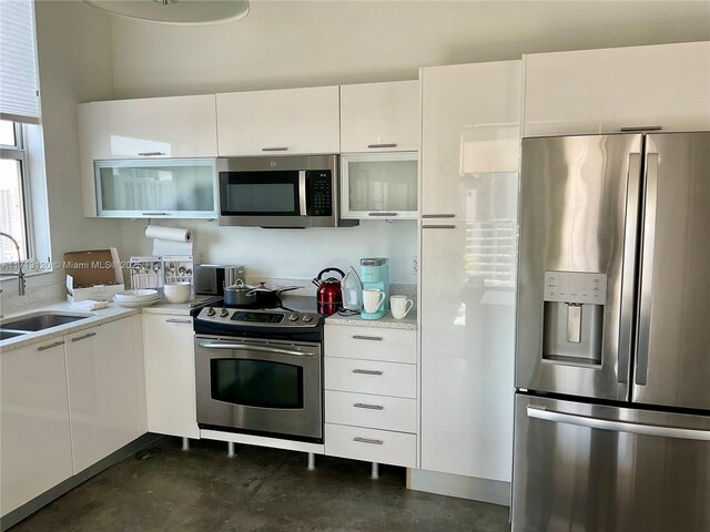 kitchen with a sink, light countertops, white cabinets, concrete flooring, and appliances with stainless steel finishes