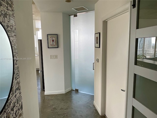 corridor featuring concrete floors, visible vents, and baseboards