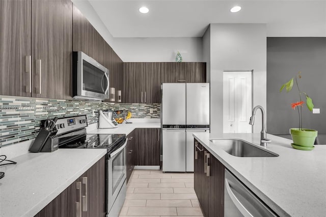 kitchen featuring backsplash, sink, light stone counters, dark brown cabinetry, and stainless steel appliances