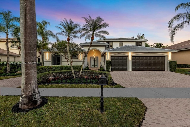 view of front of home with decorative driveway, an attached garage, and stucco siding