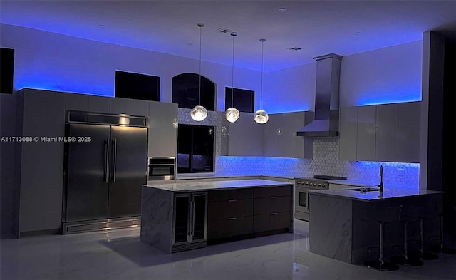 kitchen with marble finish floor, a sink, wall chimney range hood, modern cabinets, and premium appliances