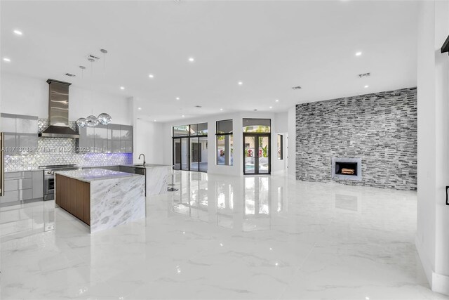 kitchen with light stone countertops, wall chimney exhaust hood, tasteful backsplash, a spacious island, and high end stainless steel range