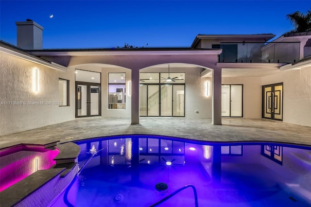 pool at twilight featuring a pool with connected hot tub, a patio area, french doors, and a ceiling fan