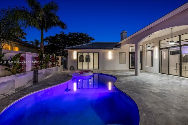 pool at twilight featuring fence, a pool with connected hot tub, ceiling fan, and a patio area