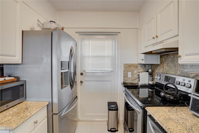 kitchen with light stone countertops, premium range hood, backsplash, white cabinets, and appliances with stainless steel finishes