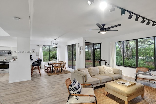 living room featuring track lighting, ceiling fan with notable chandelier, and light hardwood / wood-style flooring