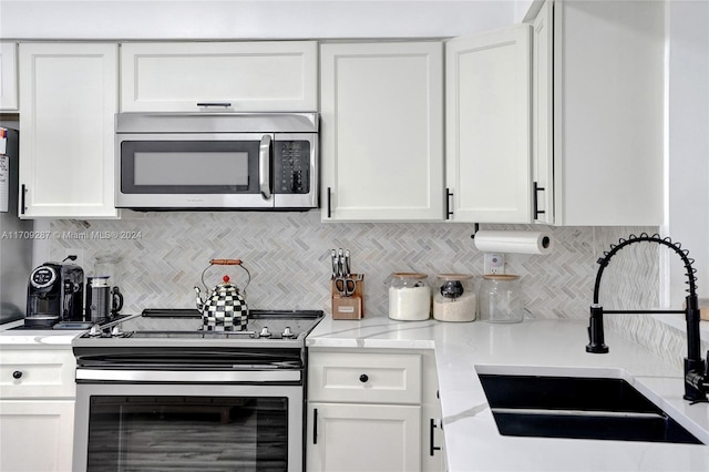 kitchen with appliances with stainless steel finishes, tasteful backsplash, light stone counters, sink, and white cabinetry