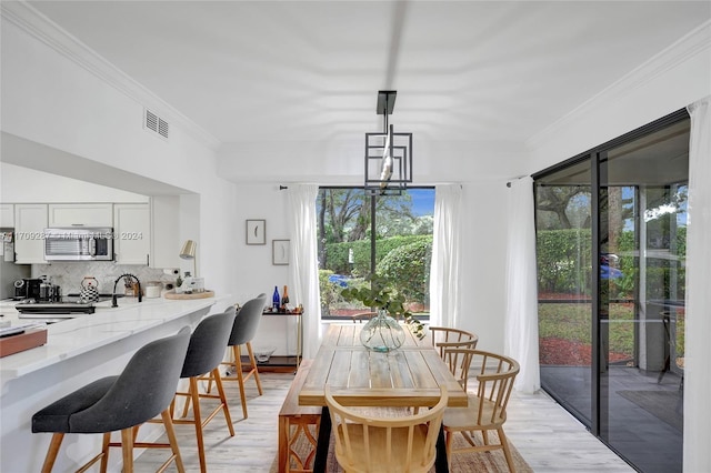 dining room featuring light wood-type flooring, ornamental molding, and sink