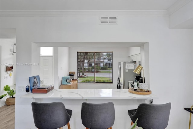 kitchen with white cabinetry, ornamental molding, light hardwood / wood-style floors, kitchen peninsula, and stainless steel refrigerator