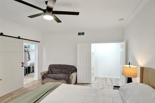 bedroom featuring a walk in closet, crown molding, light hardwood / wood-style flooring, a barn door, and a closet