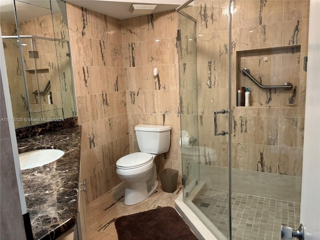 bathroom featuring tile patterned floors, toilet, a shower with door, vanity, and tile walls