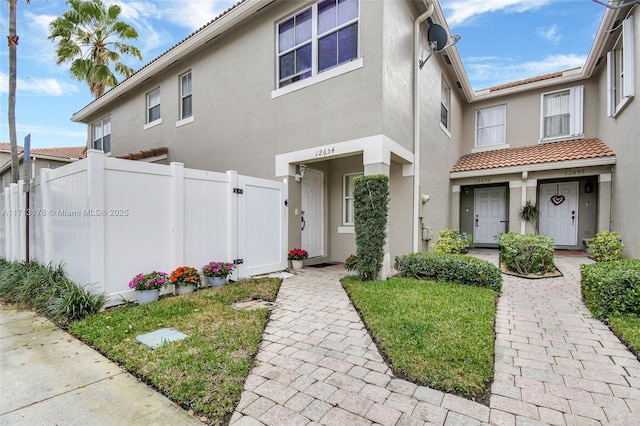 view of front of house with a gate, stucco siding, a tiled roof, and fence