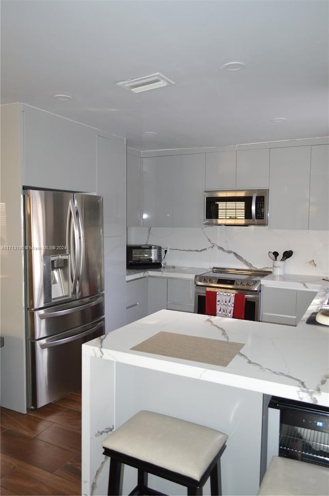 kitchen featuring dark wood-type flooring, a kitchen breakfast bar, light stone countertops, appliances with stainless steel finishes, and beverage cooler