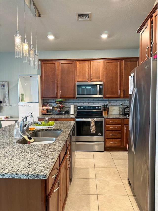 kitchen with sink, stainless steel appliances, dark stone counters, decorative light fixtures, and a kitchen island with sink