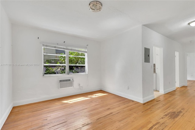 unfurnished room with electric panel, light hardwood / wood-style floors, and a wall mounted air conditioner