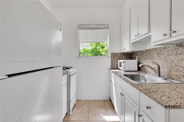 kitchen featuring white appliances, sink, decorative backsplash, light tile patterned floors, and white cabinetry