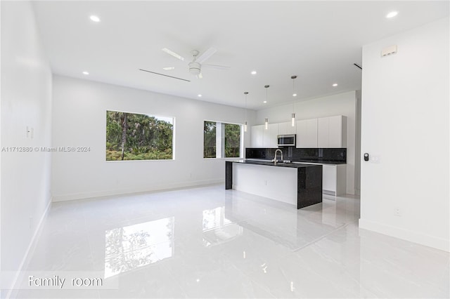 kitchen featuring white cabinetry, tasteful backsplash, hanging light fixtures, ceiling fan, and a kitchen island with sink