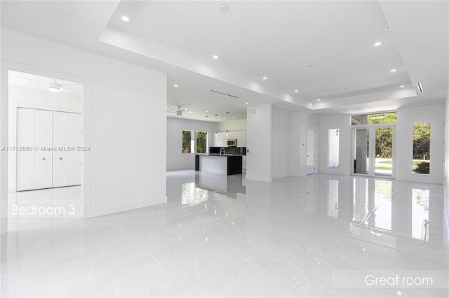 unfurnished living room with ceiling fan and a tray ceiling