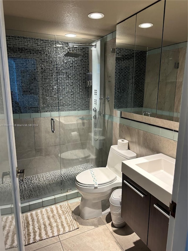 bathroom with an enclosed shower, vanity, tile walls, tile patterned flooring, and toilet