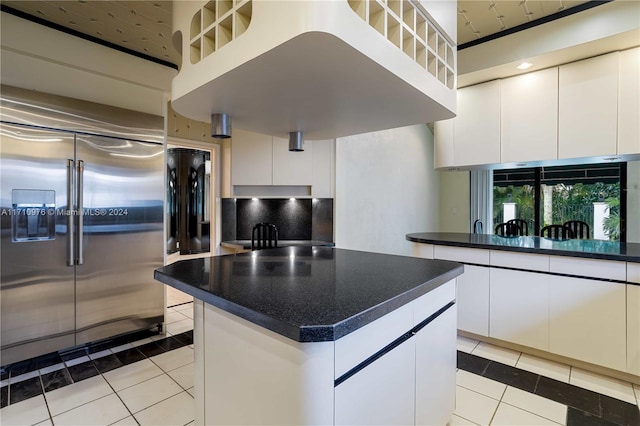 kitchen featuring decorative backsplash, light tile patterned floors, stainless steel built in fridge, white cabinets, and a kitchen island