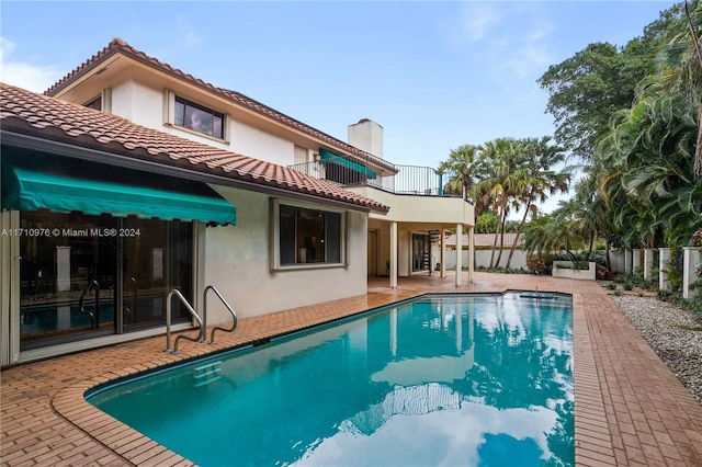 back of property featuring a patio area, a balcony, and a fenced in pool