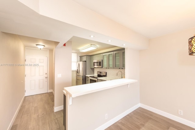 kitchen featuring light hardwood / wood-style flooring, green cabinetry, decorative backsplash, appliances with stainless steel finishes, and kitchen peninsula